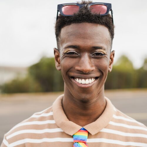 Young gay african man with makeup on looking at camera outdoor - Focus on face
