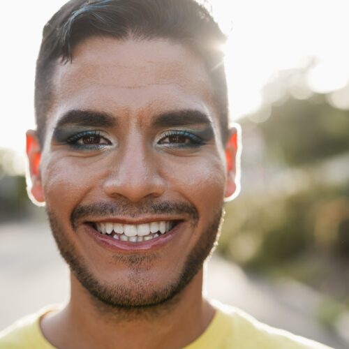 Young transgender man with makeup smiling on camera - Focus on face